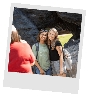 Two students taking photo in front of The Charge sculpture on campus