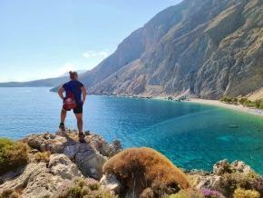 On a coastal hike, Chrissy Elliott stands with her back to the camera overlooking the Loutro Bay in Crete, Greece.