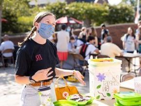 Kaley Cross works an information table outside while wearing a mask