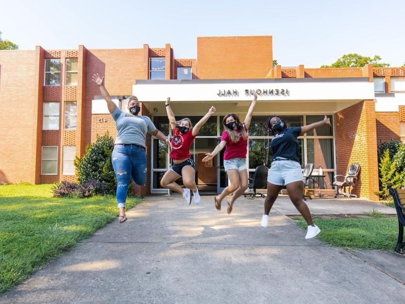 Four students jump into the air in front of Isenhour Hall. 